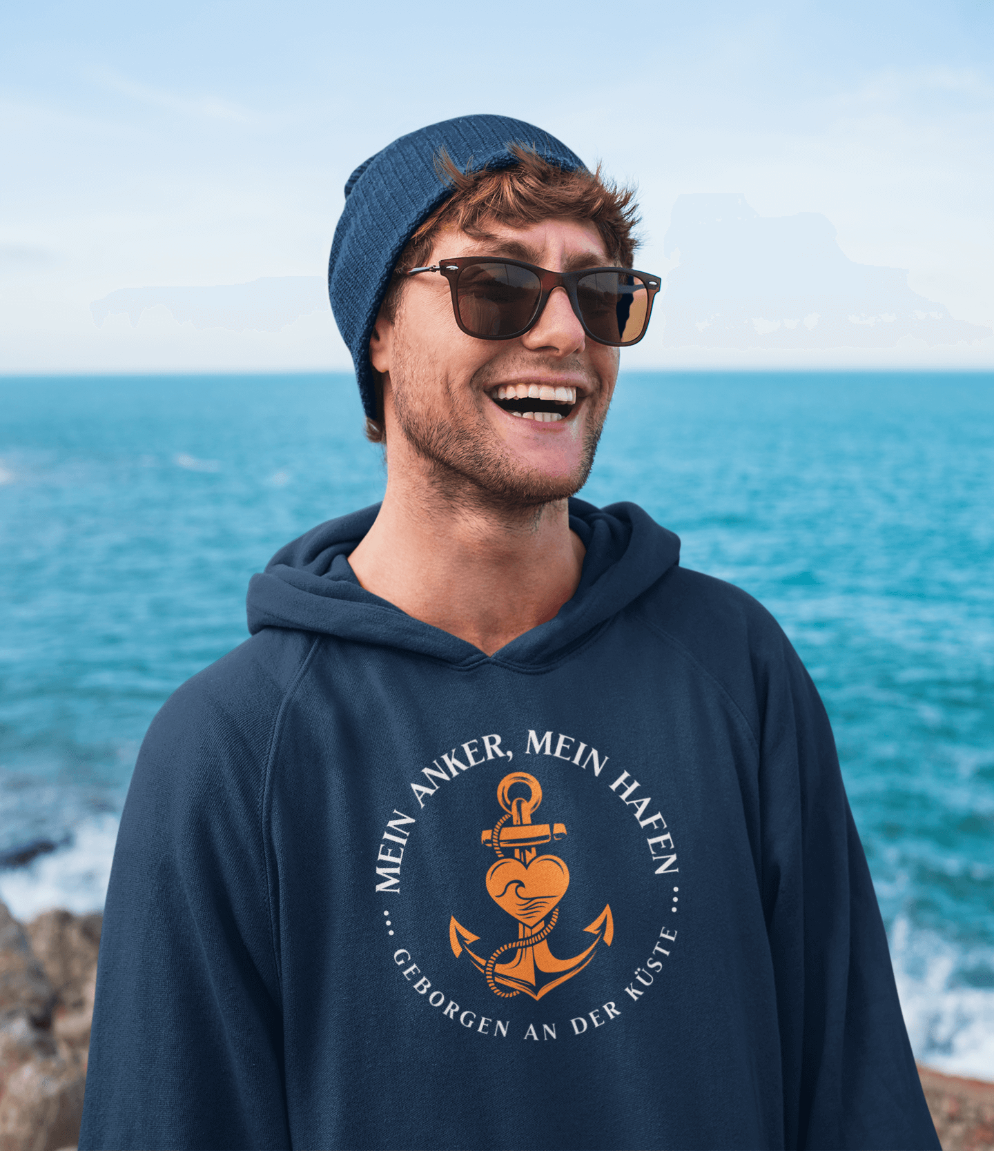 ein Mann trägt ein Mein Anker, Mein Hafen Motiv Hoodie, aus dem bereich der maritimen mode für herren, am Meer